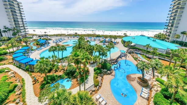 Een resort met verschillende zwembaden, palmbomen en uitzicht op het strand.