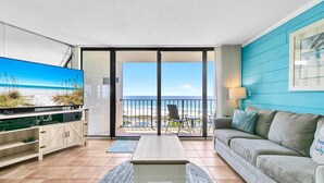 Een woonkamer met een televisie, een bank en uitzicht op het strand.