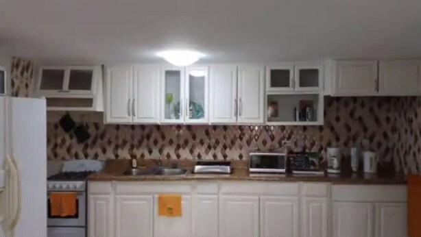 A kitchen with white cabinets, a stove, a microwave, and a patterned backsplash.
