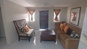 A living room with a sofa, a patterned armchair, a coffee table, and a door in the background.
