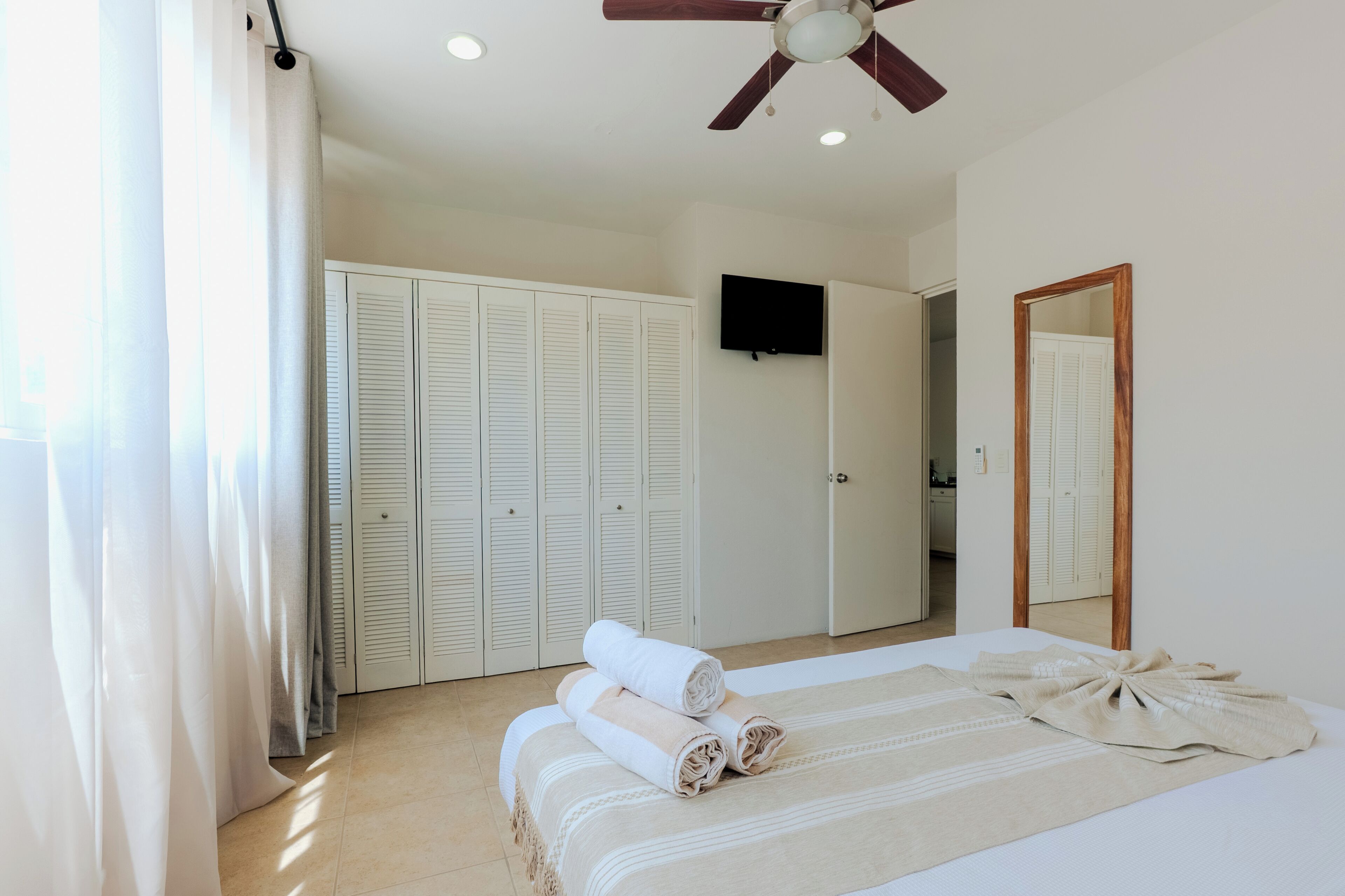 A bedroom with a bed, a ceiling fan, a TV, and a wardrobe.