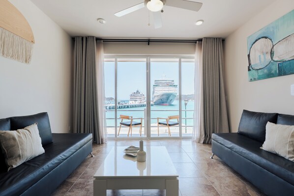 Una sala de estar moderna con dos sofás negros, una mesa de centro de vidrio y vistas a un crucero a través de grandes ventanales.