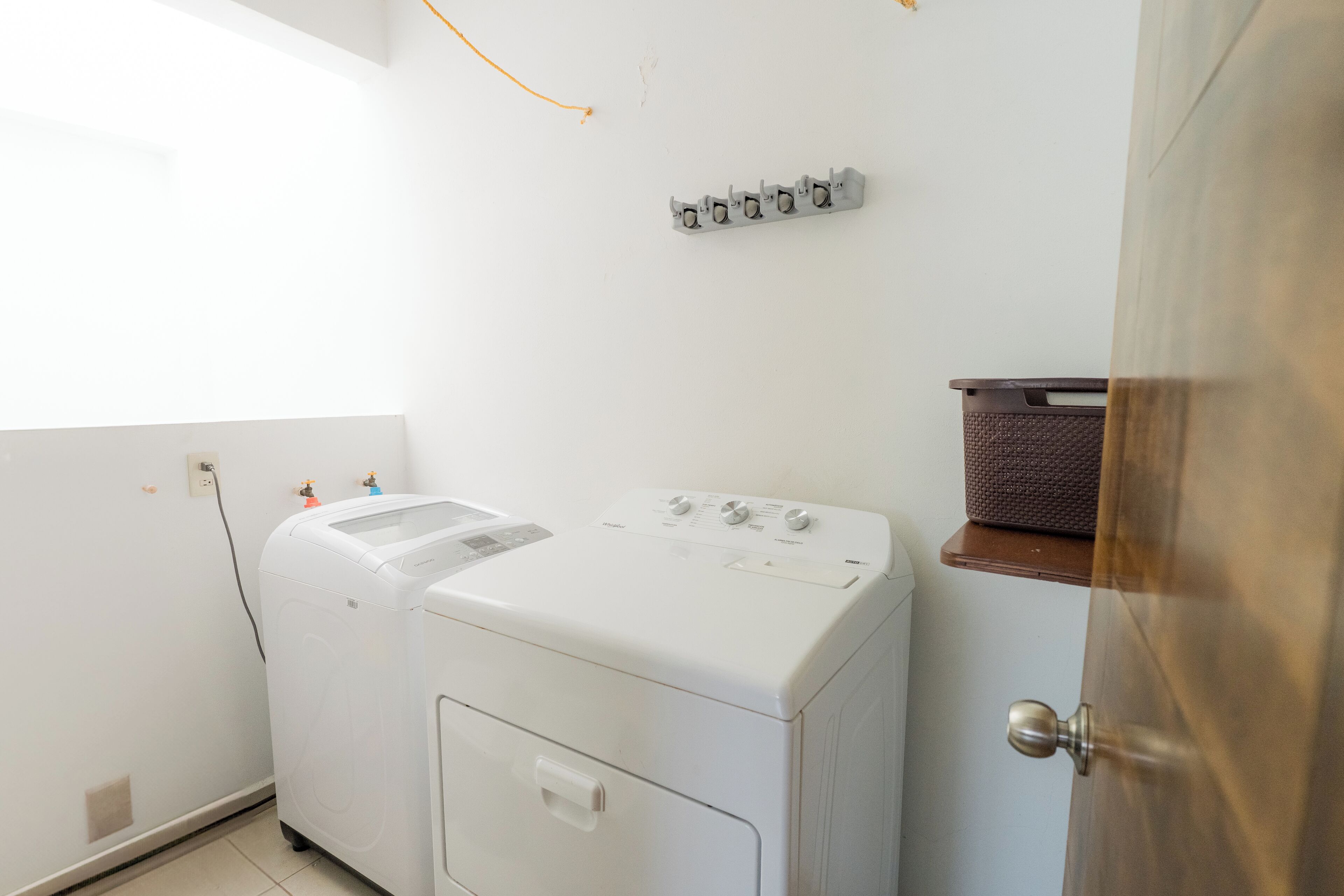 A laundry area with a white washing machine and dryer, a small shelf with a basket, and a door with a round knob.