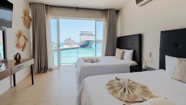 Ein Hotelzimmer mit zwei Betten, einem Fernseher, einem Schreibtisch und Blick auf ein Kreuzfahrtschiff.