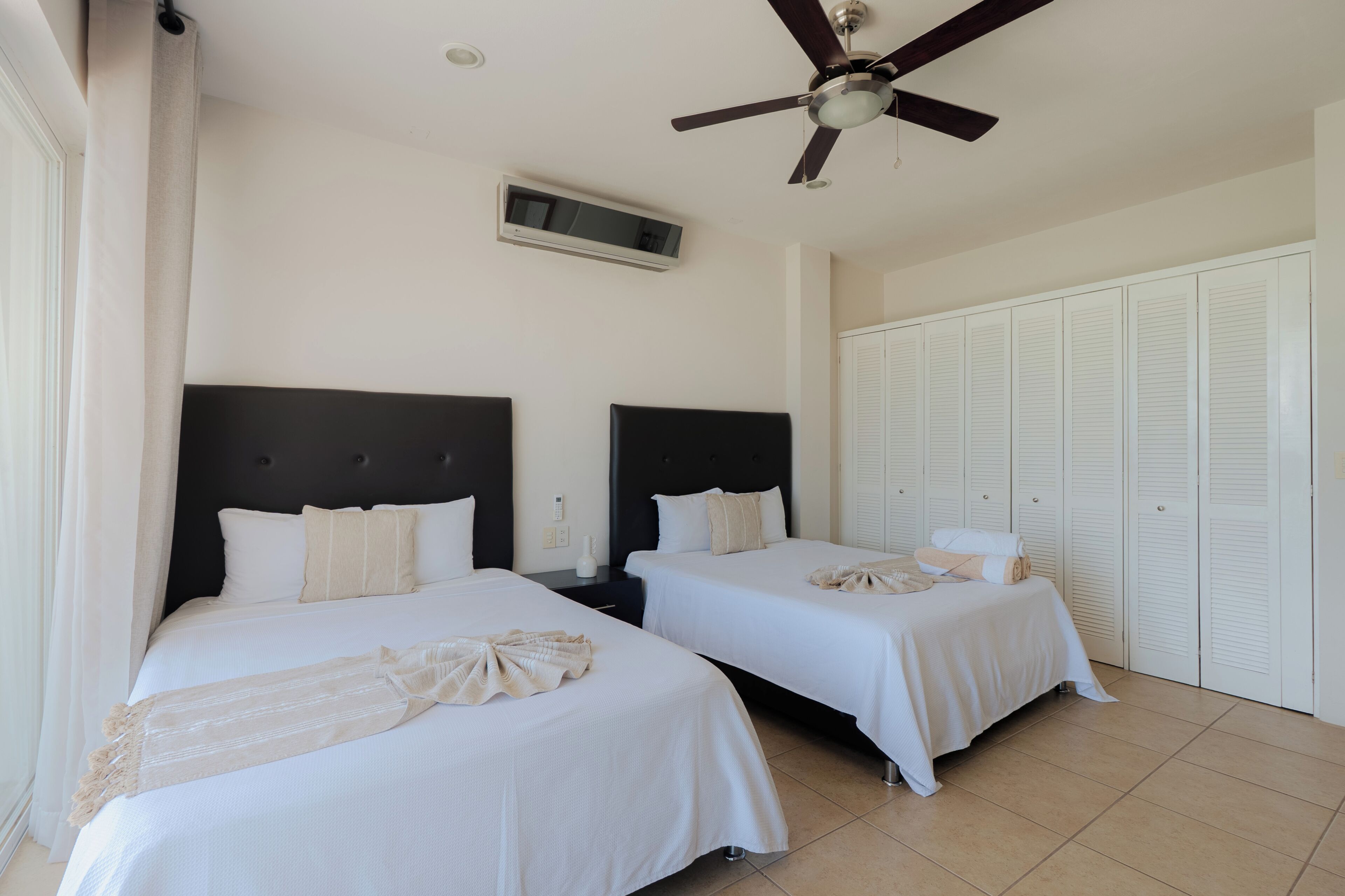 Habitación de hotel con dos camas, ventilador de techo, televisión y armario.