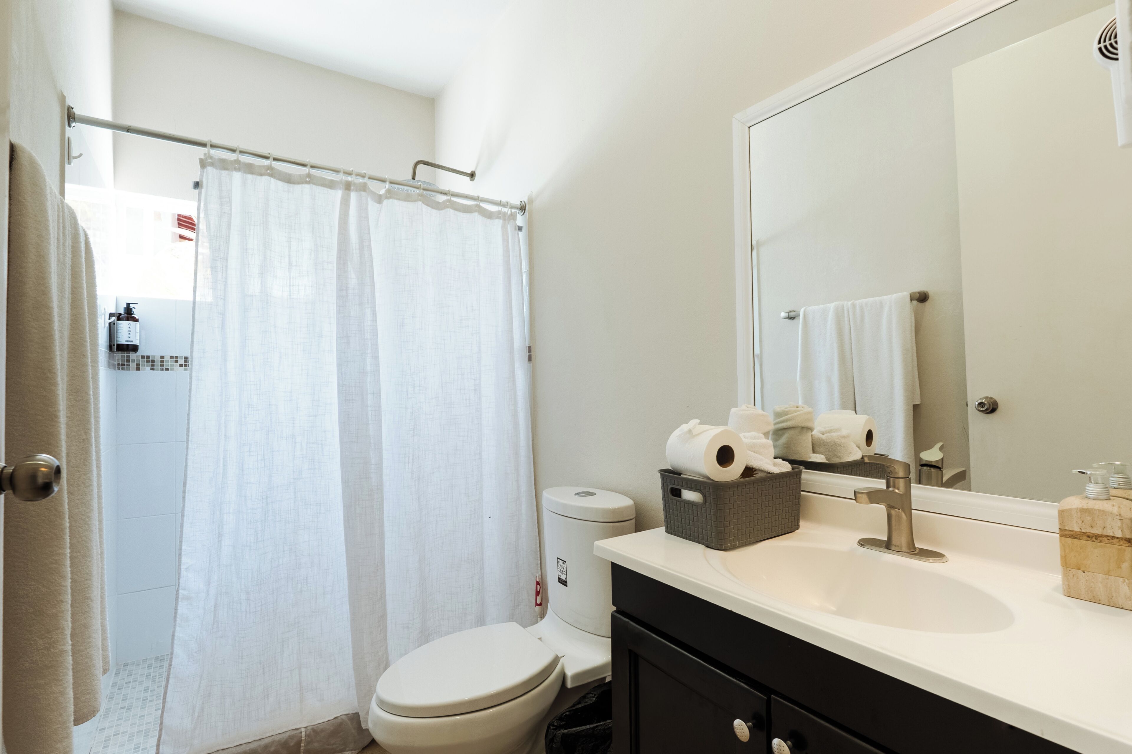 A bathroom with a toilet, a sink, a mirror, a shower curtain, and a towel rack.