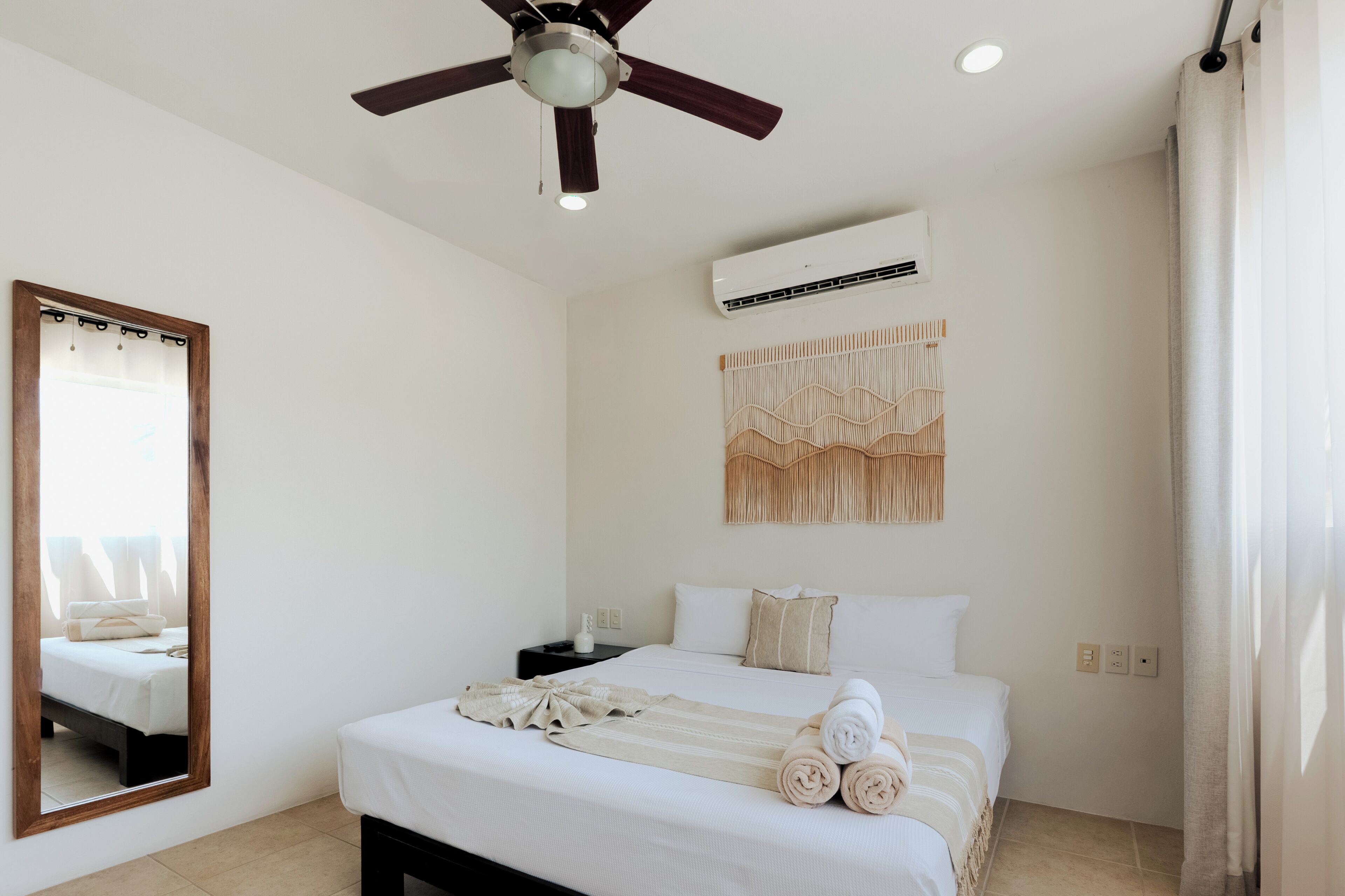 Ein Schlafzimmer mit einem Bett, einem Deckenventilator, einer Klimaanlage, einem Nachttisch und einem Wanddekor.