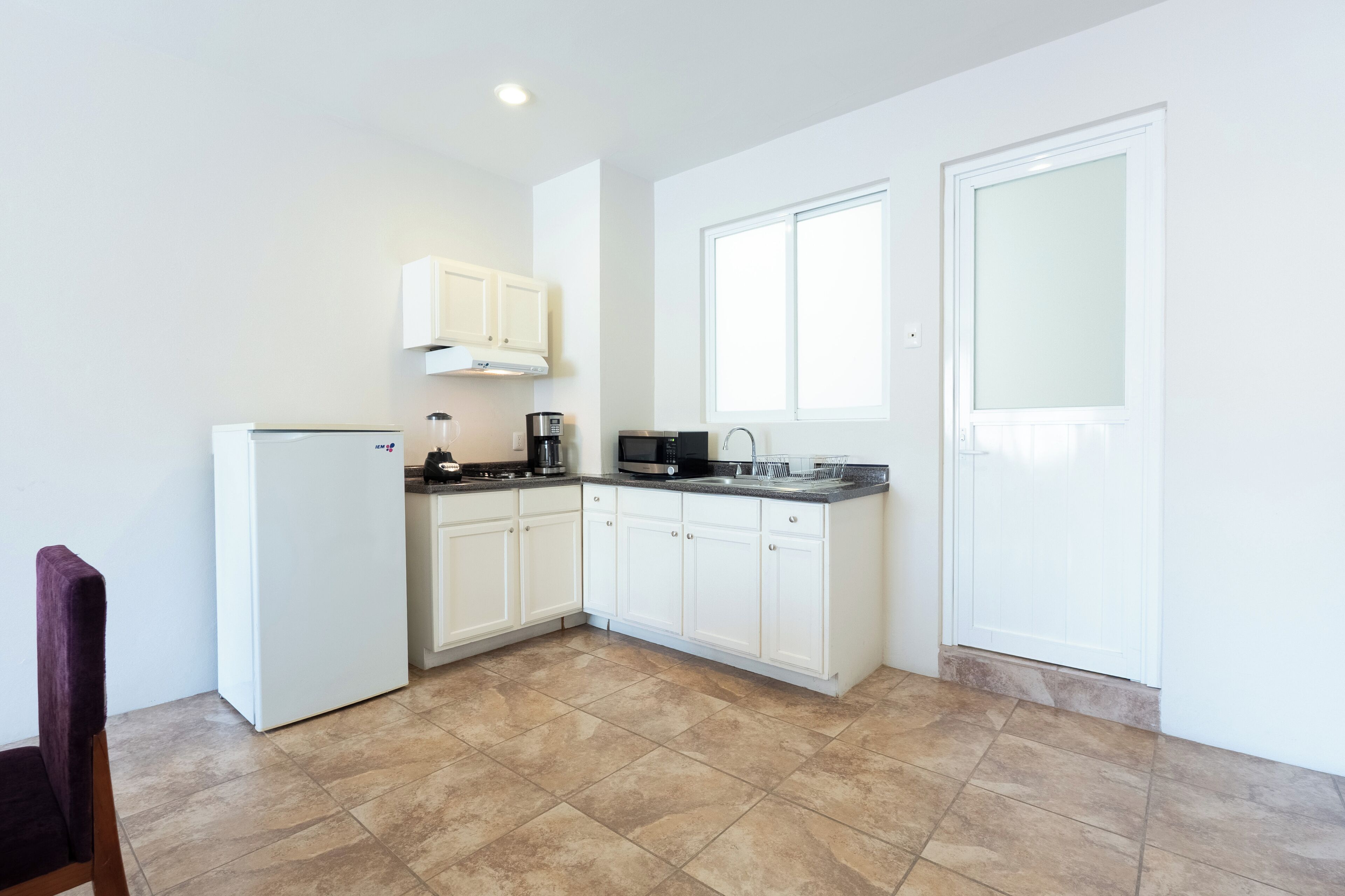 Una cocina con armarios blancos, un refrigerador, una cafetera y un microondas.