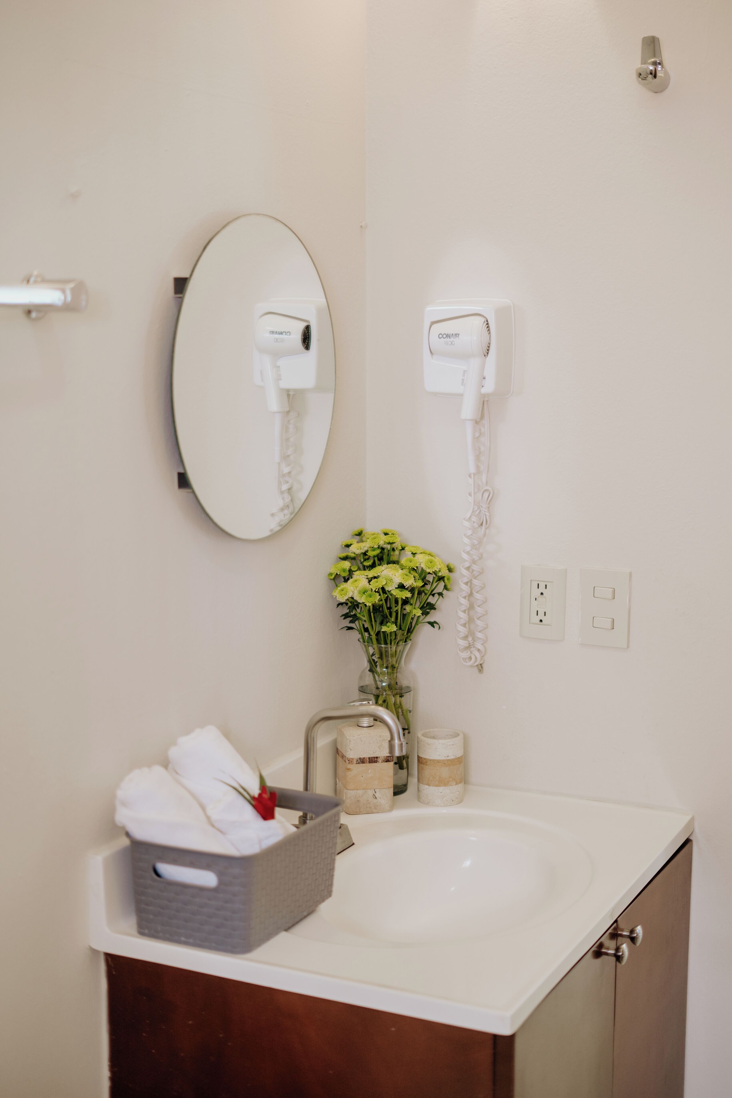 A bathroom with a white sink, a mirror, a vase with flowers, a towel rack, and a telephone.