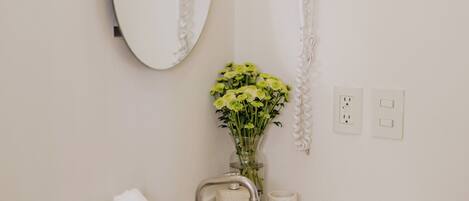 Un baño con un lavamanos blanco, un espejo, un jarrón con flores, un perchero y un teléfono.