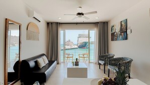 A modern living room with a black sofa, patterned chairs, a coffee table, and a view of a cruise ship through large windows. - Suites La Playa (Santa Maria Huatulco)