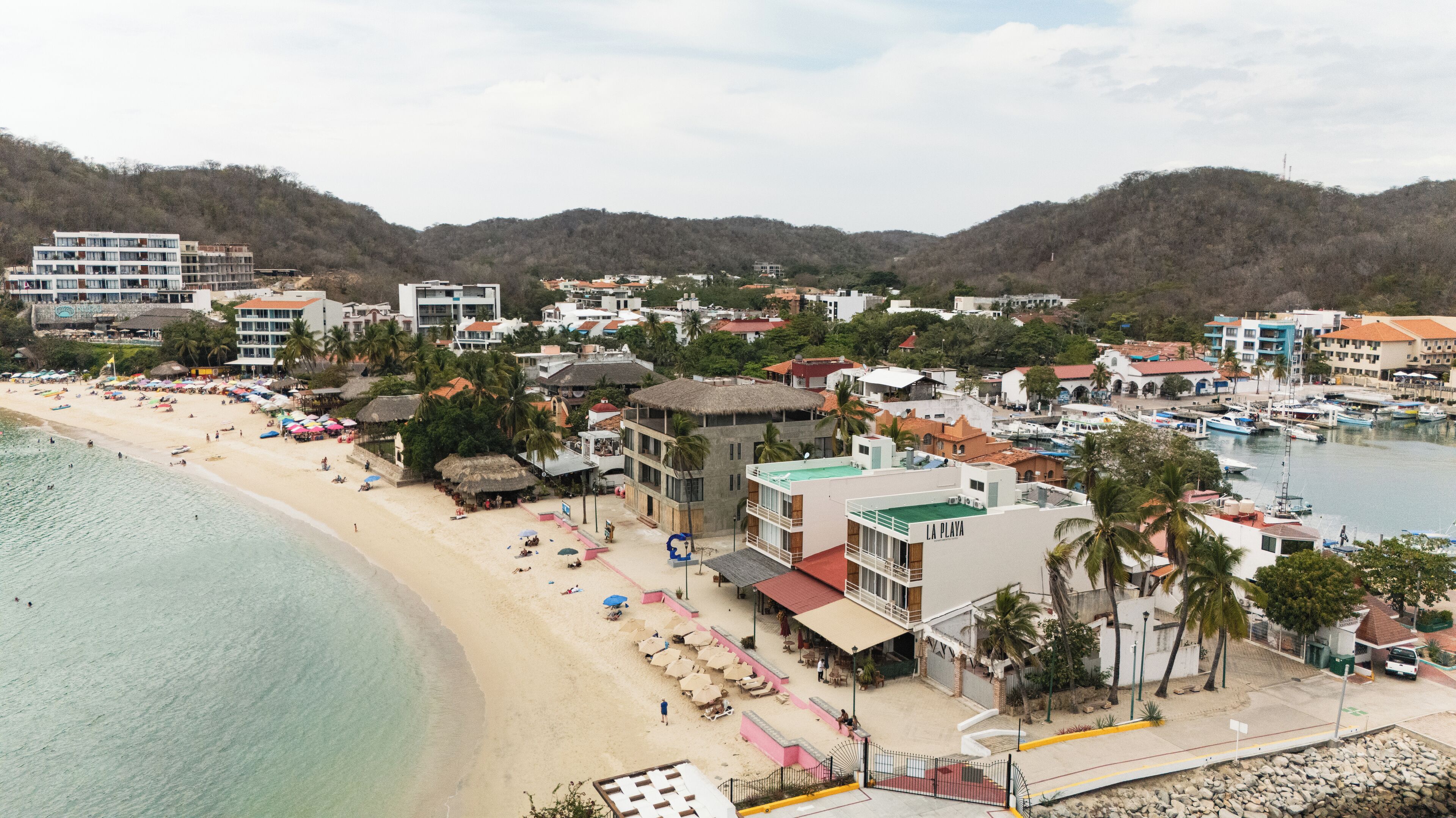 A coastal town with a beach, a marina, and buildings with balconies overlooking the sea.
