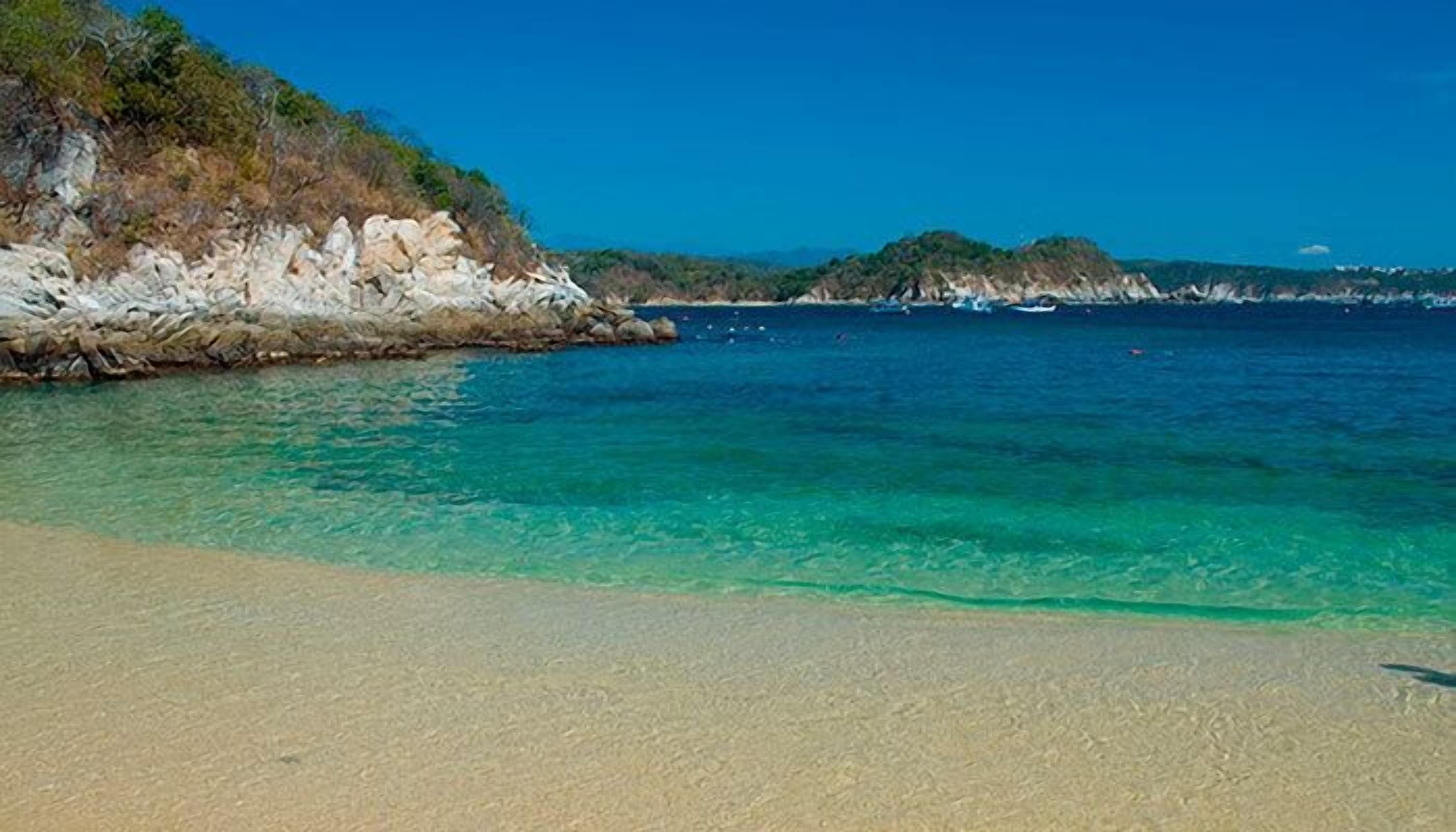 Una playa con aguas turquesas transparentes, orilla de arena y acantilados rocosos.