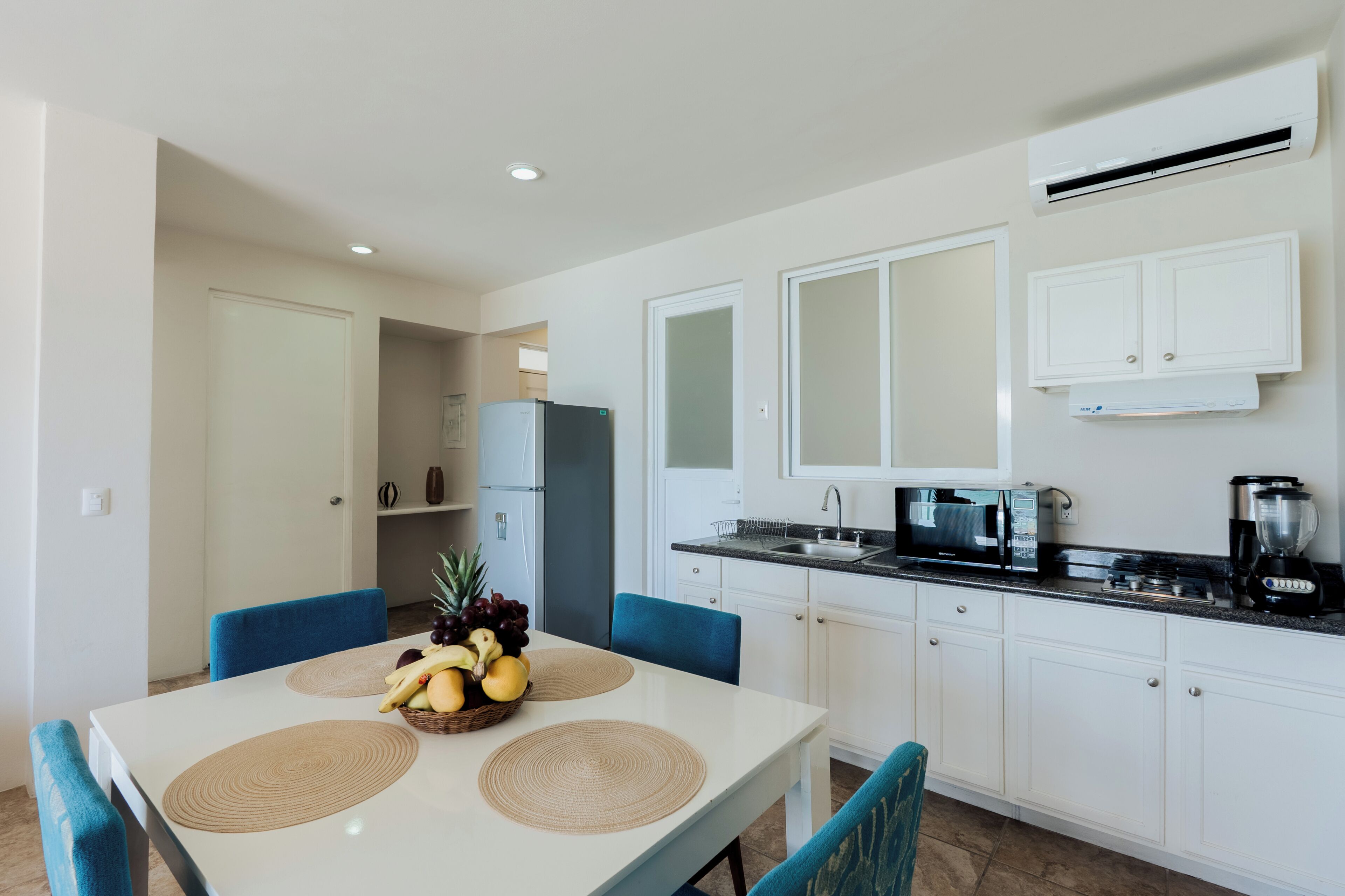A modern kitchen with white cabinets, a black countertop, and a dining table with blue chairs.