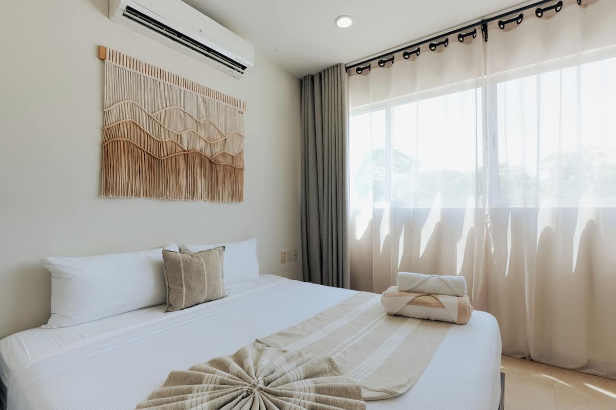 Camera d'albergo con un letto grande, un condizionatore d'aria a muro, una finestra con tende e un elemento decorativo.