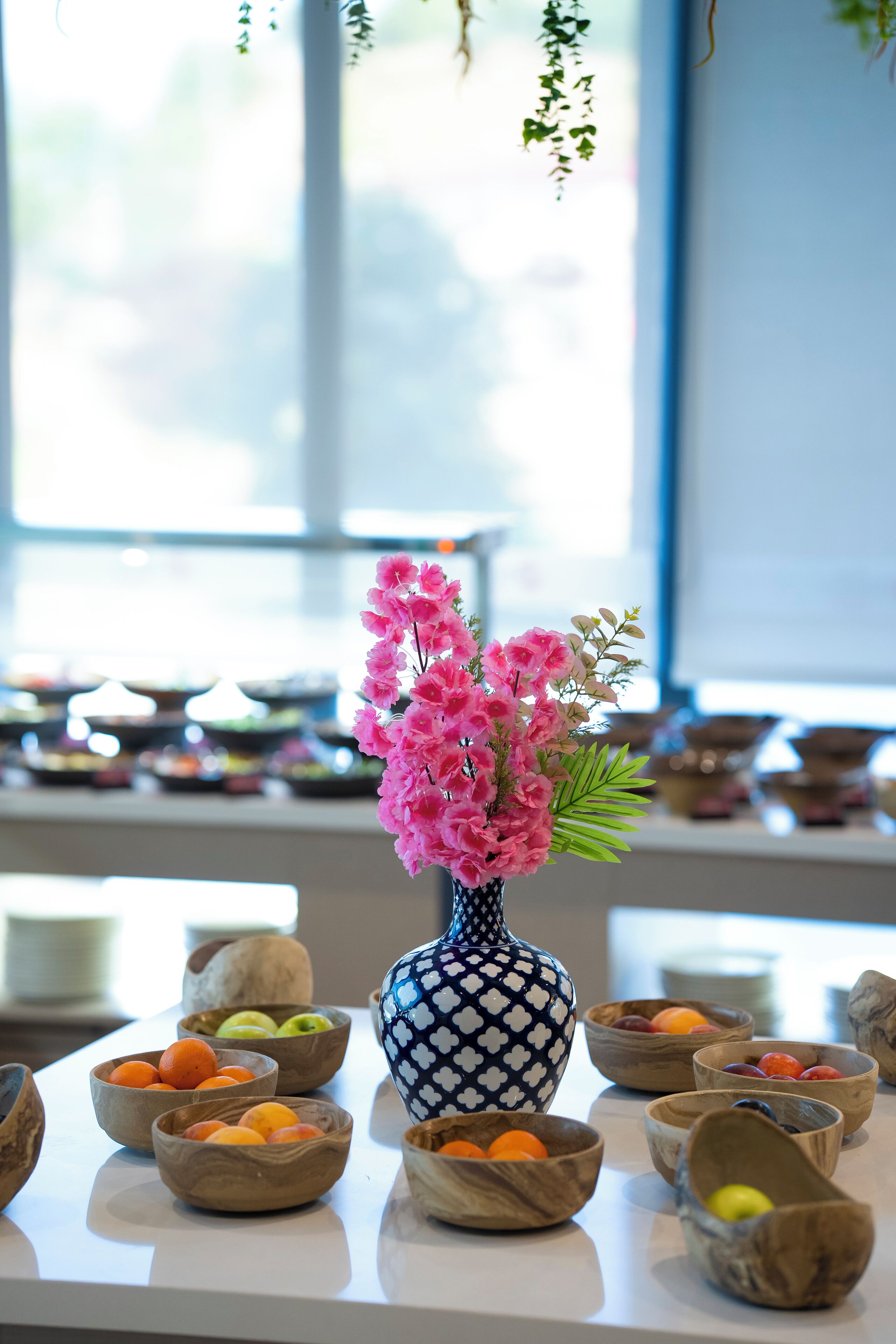 A table with a vase of pink flowers and various wooden bowls containing fruits.