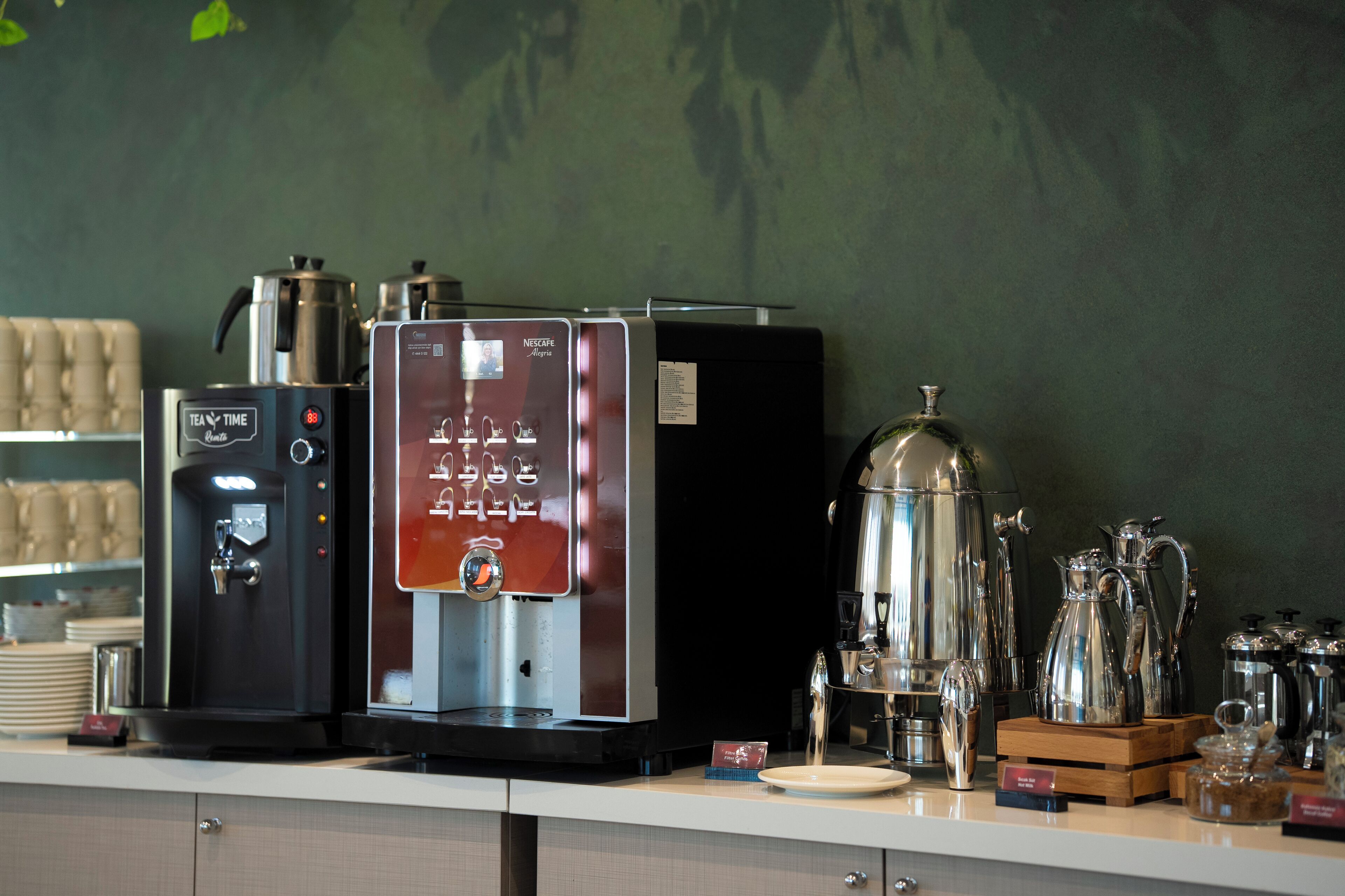 Una estación de café con máquina de Nescafé, dispensador de agua y diferentes cafeteras y recipientes.
