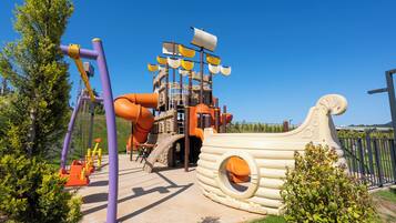 Un parque infantil con una estructura de juego temática náutica, que incluye toboganes y zonas de escalada.