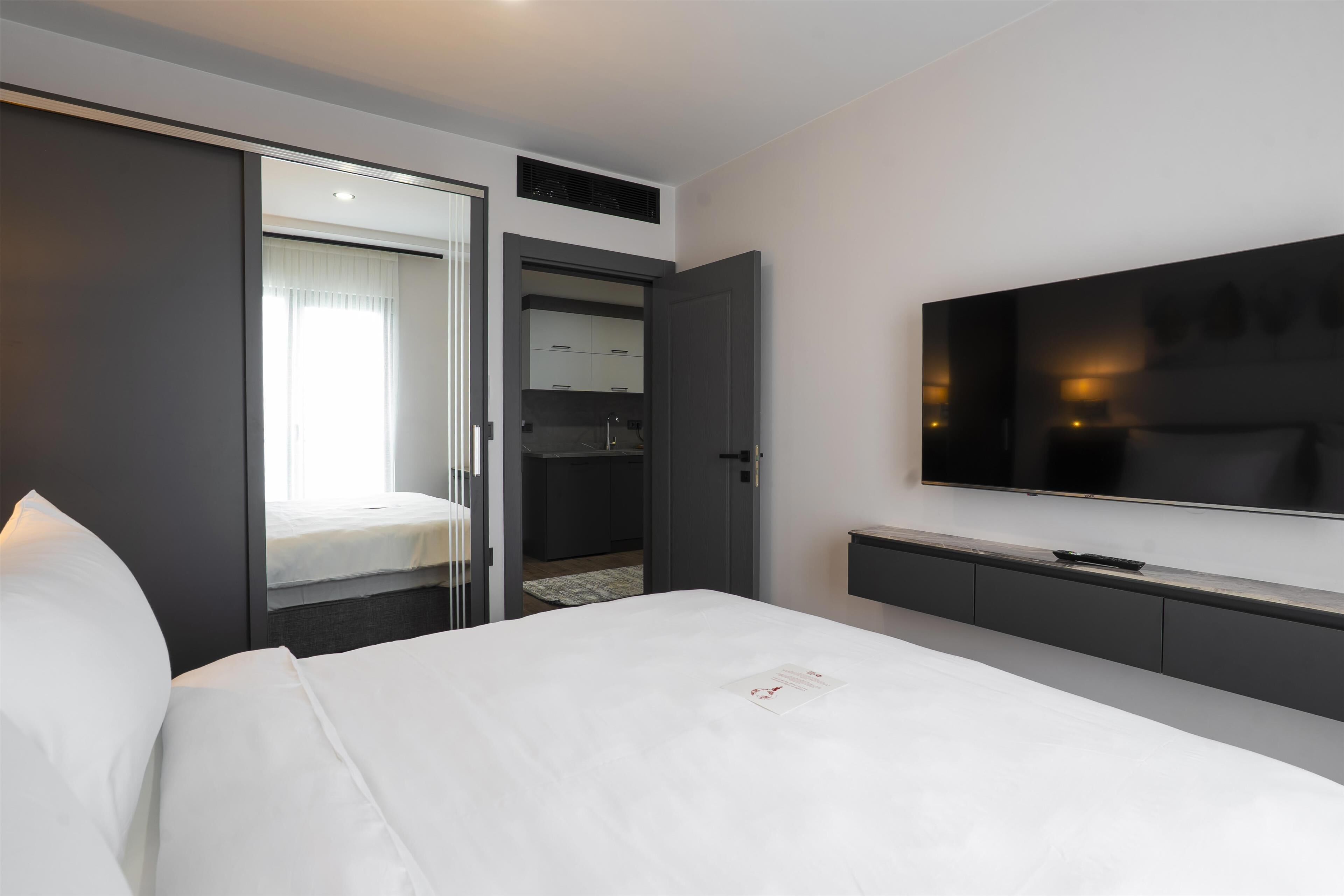 Een moderne hotelkamer met een groot bed, een flatscreen televisie aan de muur, een inloopkast en een schuifdeur naar een badkamer.