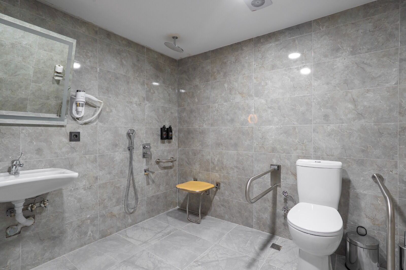 A modern bathroom with a sink, toilet, shower, and a small wooden stool.