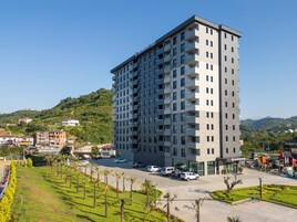 Un hotel alto y moderno con varios balcones, un estacionamiento y vistas a un paisaje montañoso.