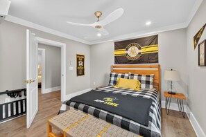 Un dormitorio con una cama, un ventilador de techo, una mesita de noche y una pared con una bandera.