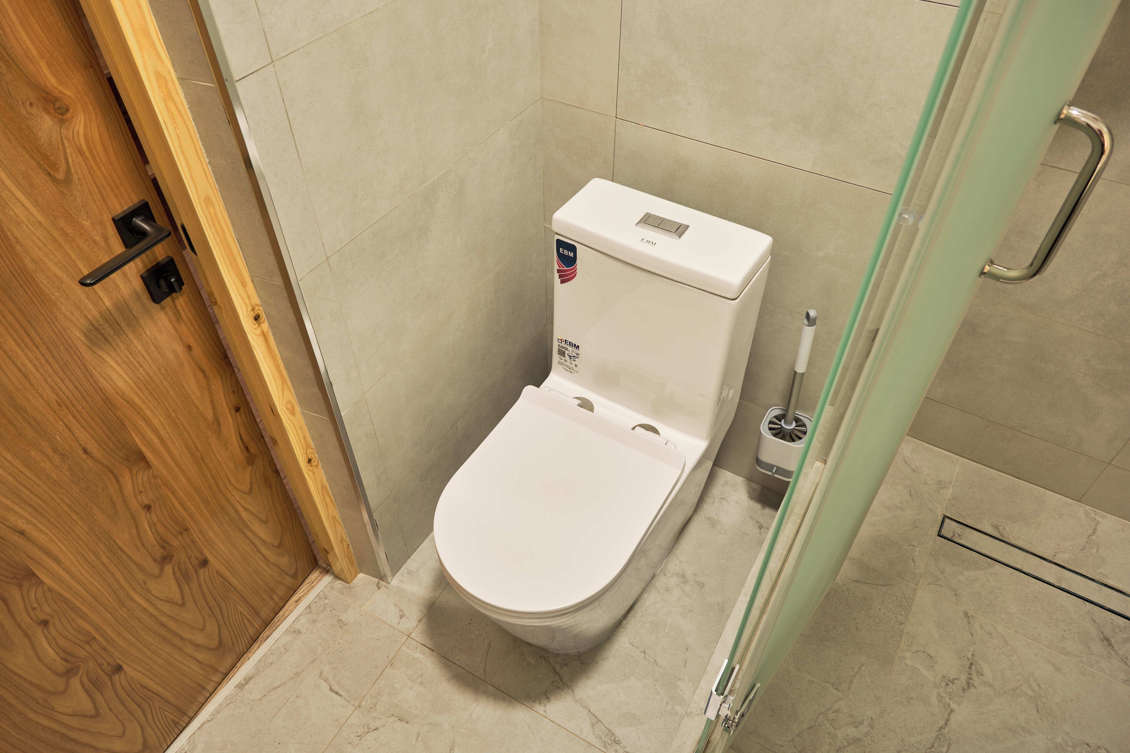 A bathroom with a white toilet, a wooden door, and a glass shower enclosure.
