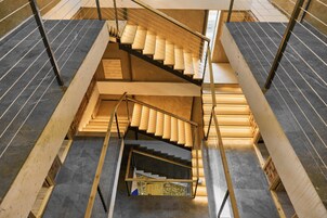 Una escalera de varios niveles con escalones de madera y barandillas de metal, rodeada de paredes de piedra y un suelo de baldosas.