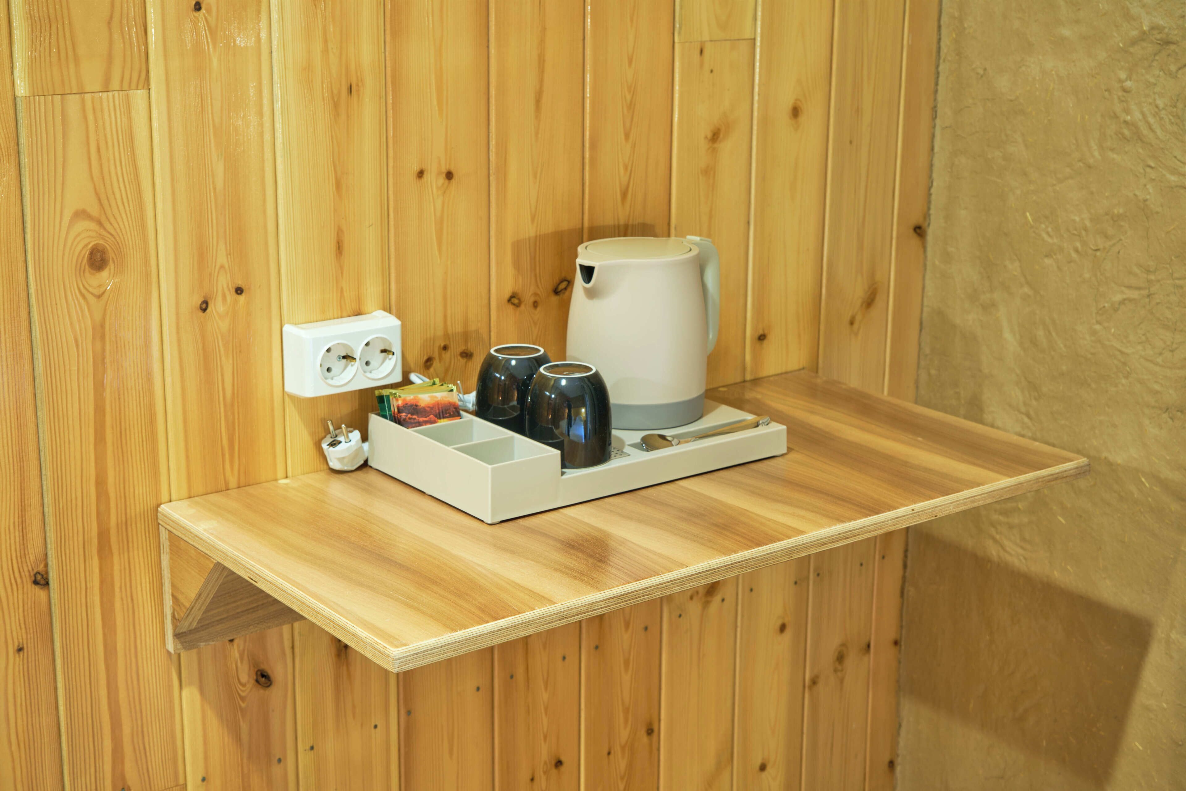 A wooden shelf with a coffee maker, cups, and a power outlet.