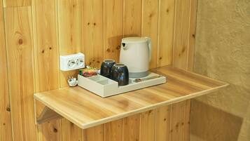 A wooden shelf with a coffee maker, cups, and a power outlet.