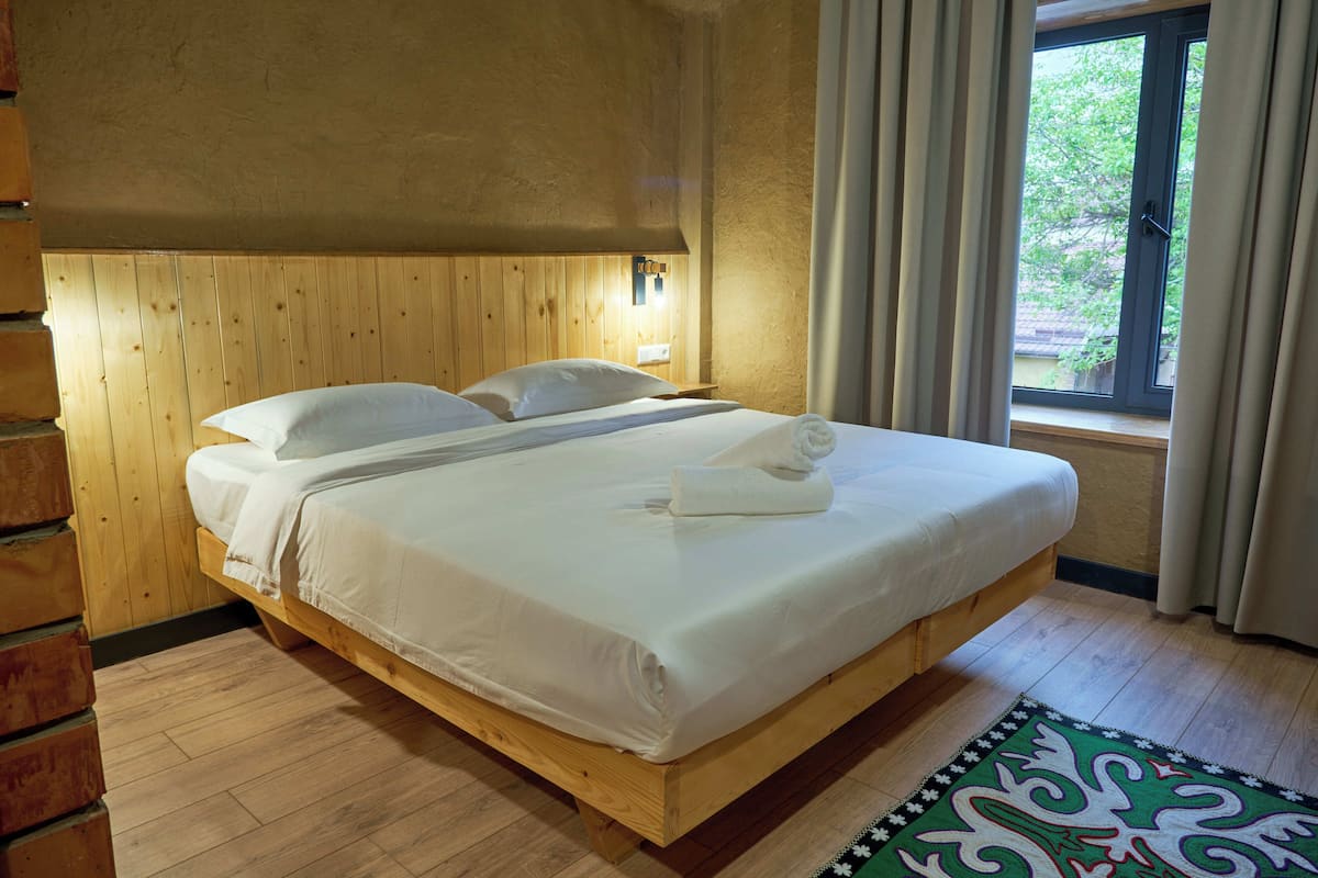 A wooden bed with white linens, a bedside table, and a window with curtains.