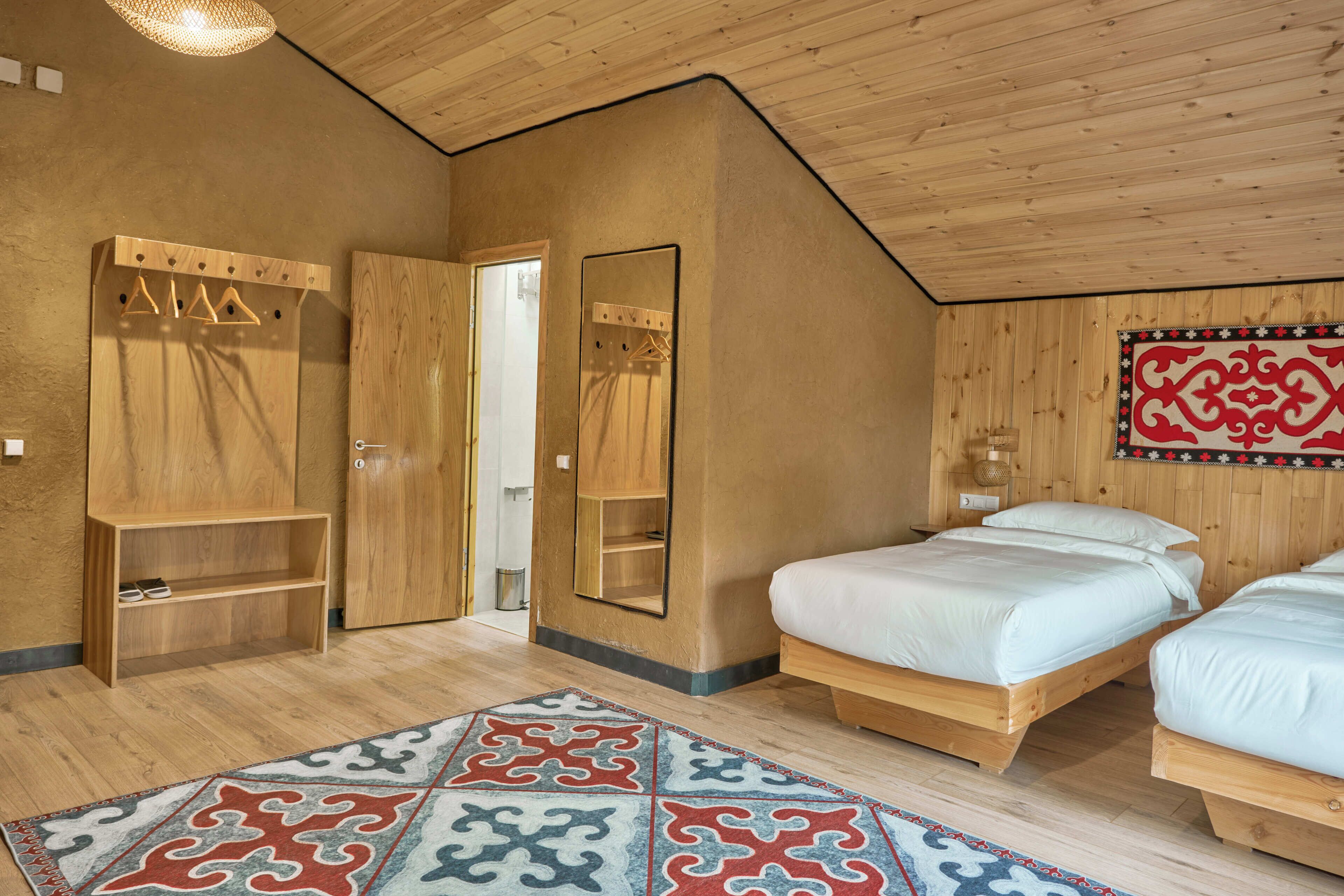 A room with two wooden beds, a wooden wardrobe, a mirror, and a patterned rug.