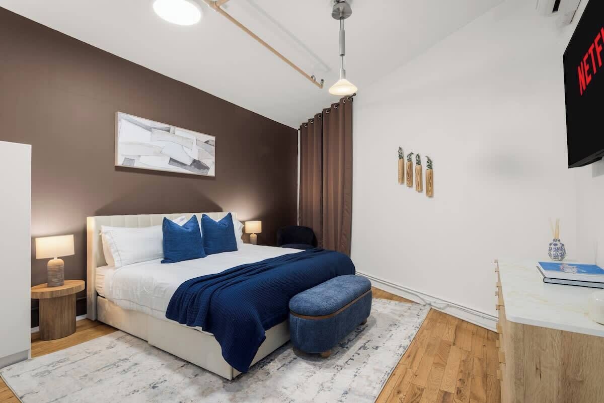 A modern bedroom with a bed, bedside lamps, a wall-mounted artwork, a desk with a chair, and a TV.