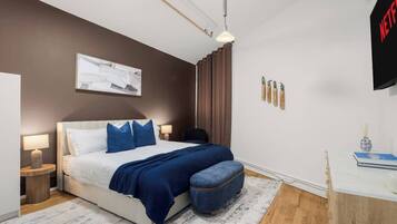 A modern bedroom with a bed, bedside lamps, a wall-mounted artwork, a desk with a chair, and a TV.