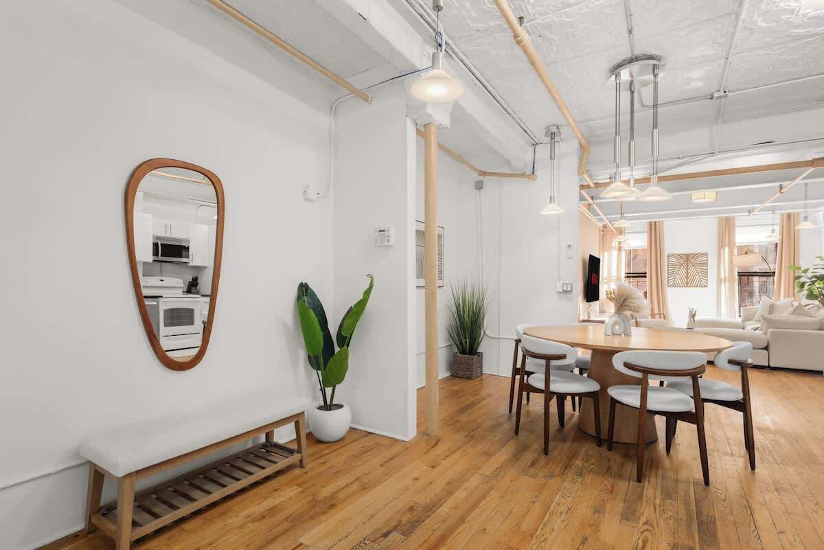 A modern interior with a wooden floor, white walls, a round dining table with chairs, a bench, and a potted plant.