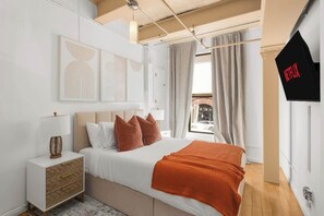 Quarto com cama, mesa de cabeceira e televisão presa à parede.