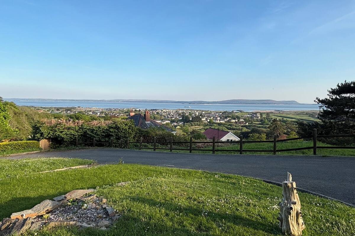 A coastal view with a grassy area, a wooden fence, and a distant town.