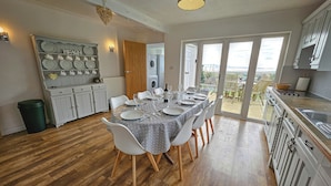 A dining area with a table set for six, wooden flooring, and a view through a glass door to an outdoor patio. - Raphael House (Burry Port)