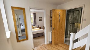 A hallway with wooden flooring, a mirror, a door leading to a bedroom, and a shower area. - Raphael House (Burry Port)