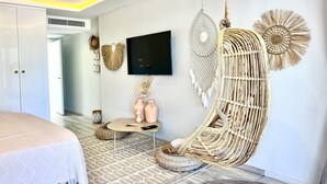 Une chambre moderne avec un fauteuil suspendu, un téléviseur et des œuvres d’art décoratives au mur.
