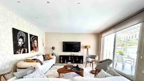 Un salon moderne avec un grand canapé, un téléviseur à écran plat et une vue sur l’extérieur.