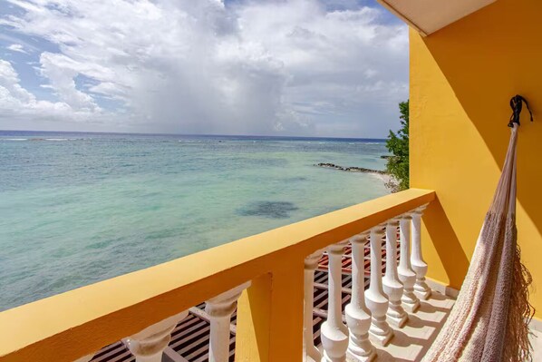 Een balkon met uitzicht op de oceaan, een hangmat en een gele muur.