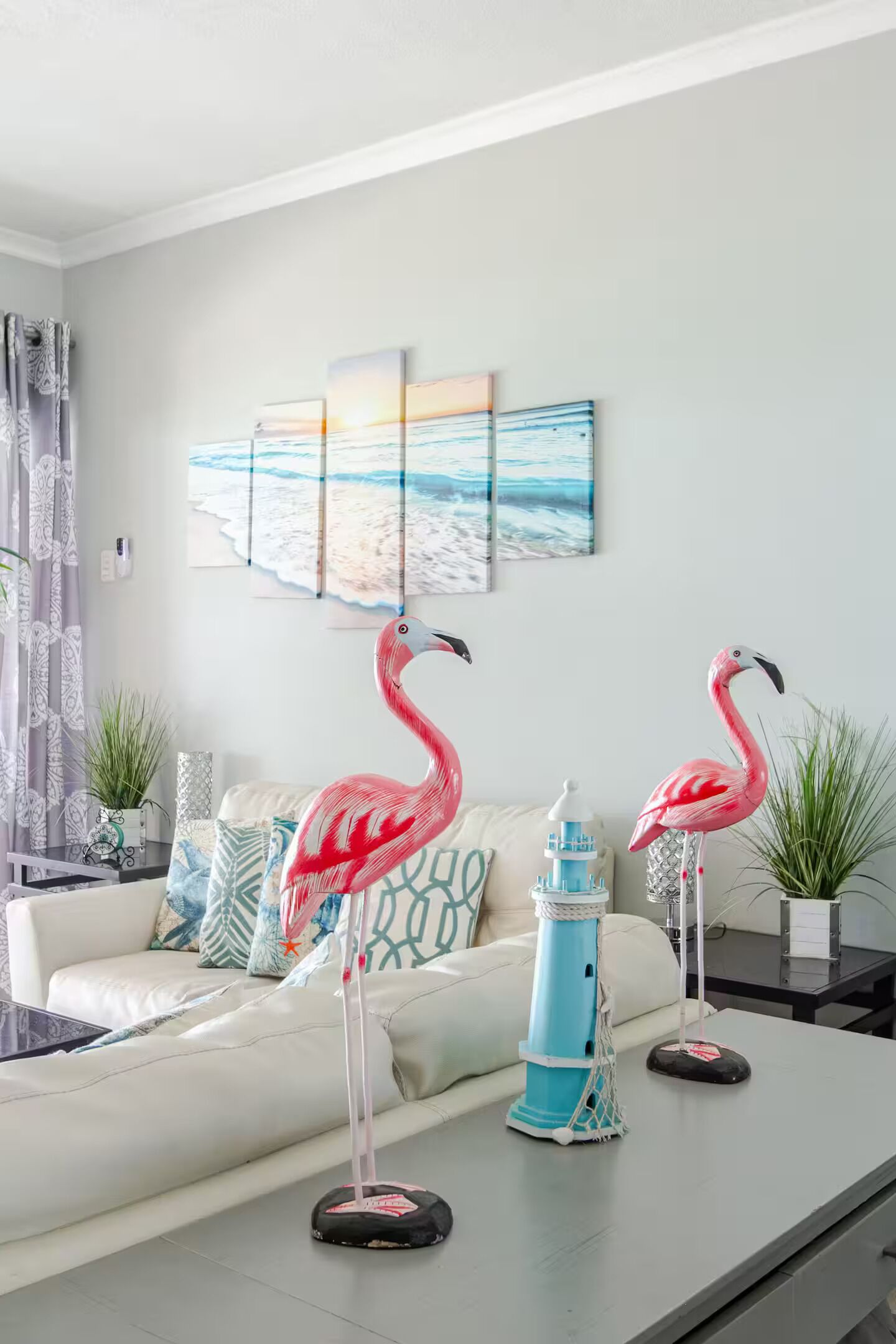 A living room with a white sofa, decorative pillows, a blue lighthouse, and two pink flamingo statues.