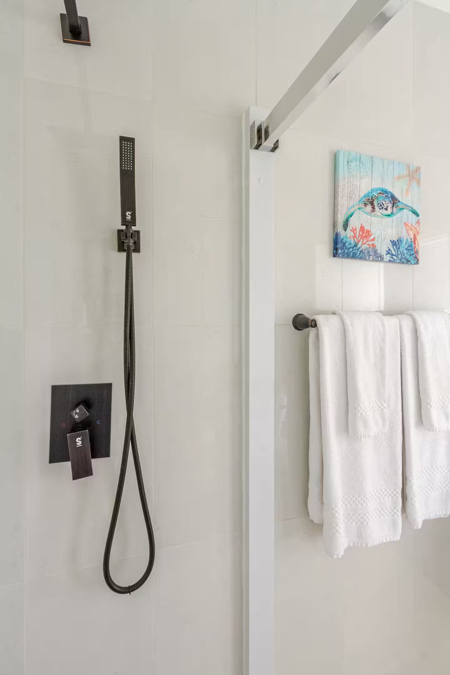 A modern bathroom with a shower, a towel rack with white towels, and a colorful artwork on the wall.