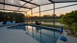 A swimming pool with lounge chairs and a view of a lake at sunset. - Magnificent Lake View - Spacious 5-bdrm Pool Home - Close to Disney (Kissimmee)