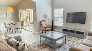 A modern living room with a sofa, coffee table, TV, and dining area. - Magnificent Lake View - Spacious 5-bdrm Pool Home - Close to Disney (Kissimmee)