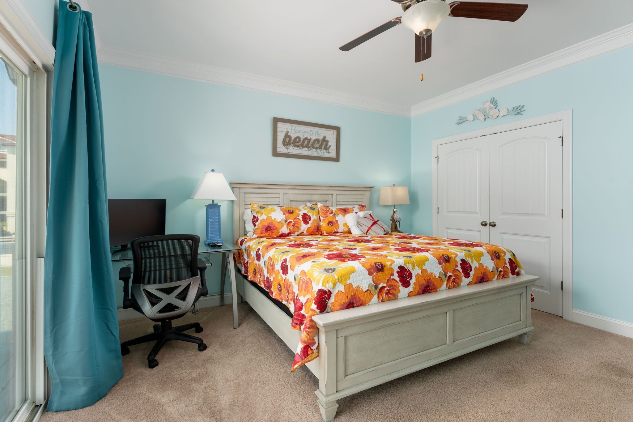 A bedroom with a bed, desk, chair, and a ceiling fan.