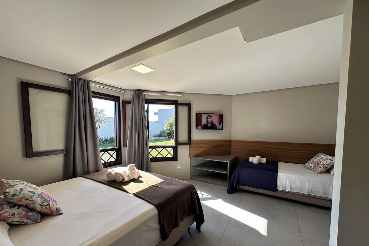 Habitación de hotel con dos camas, televisión y balcón con cortinas.