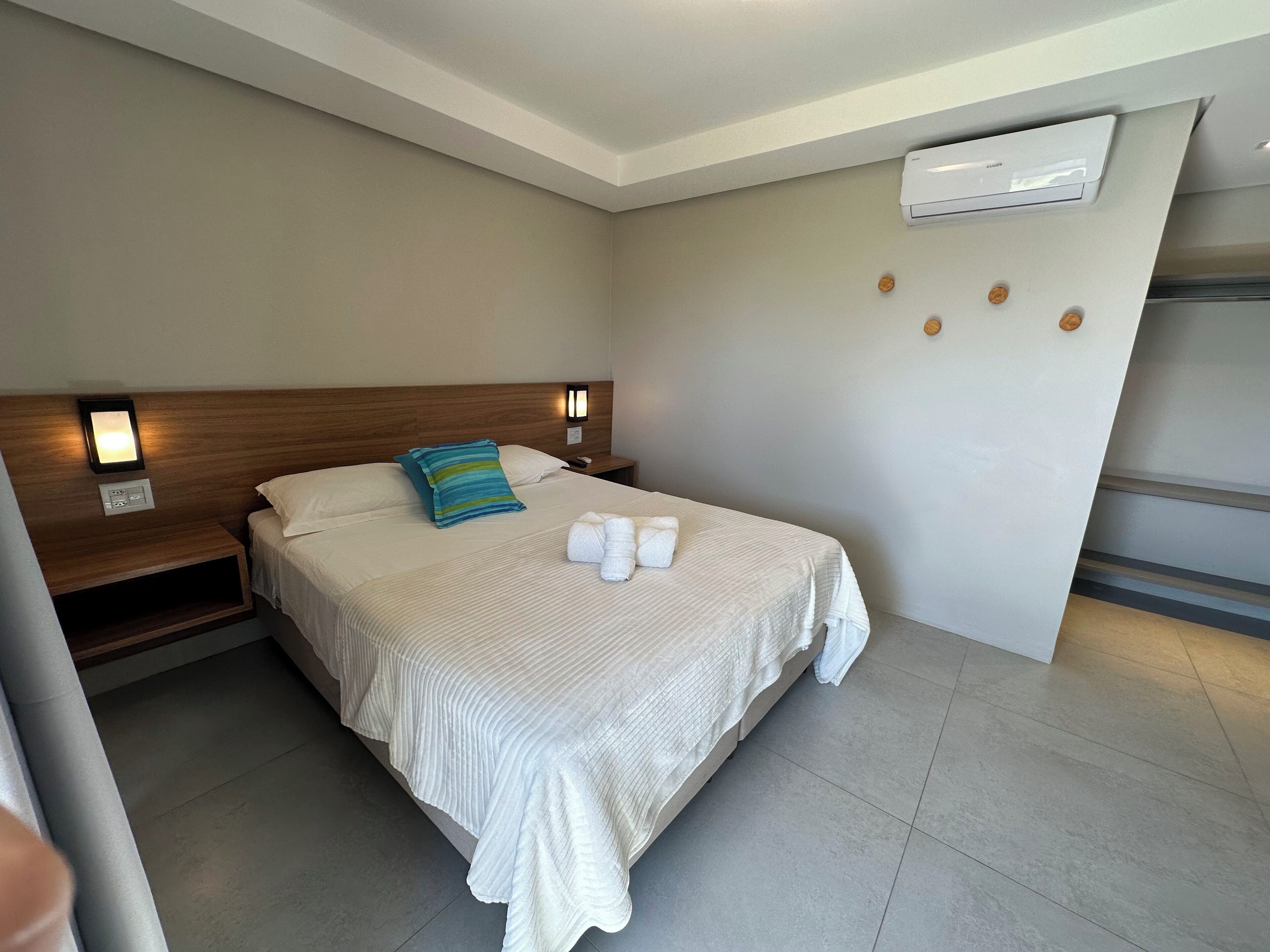 A hotel room with a bed, a nightstand, a wall-mounted air conditioner, and a small shelf.