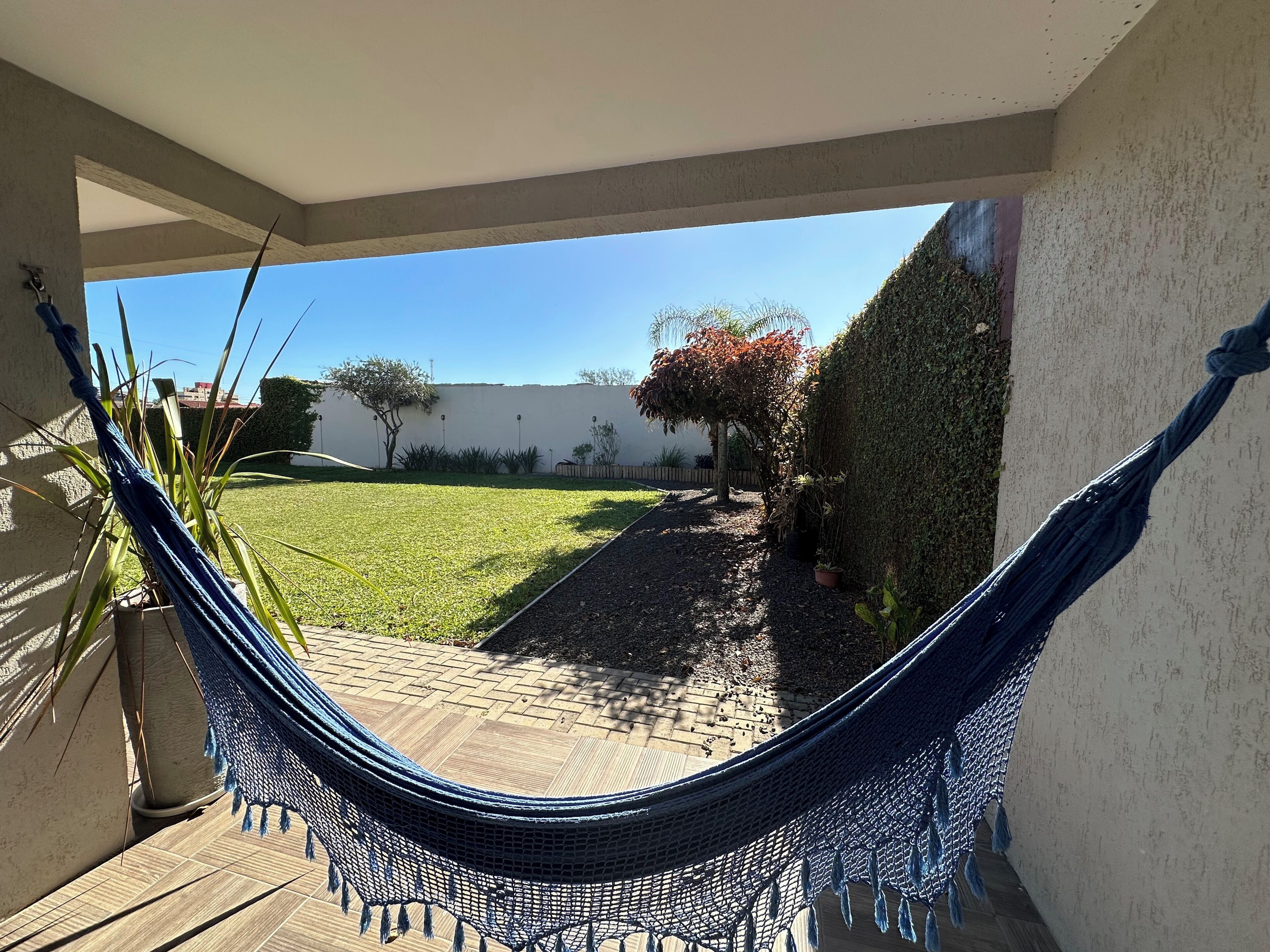 A hammock in a covered outdoor area with a view of a grassy yard and a hedge.